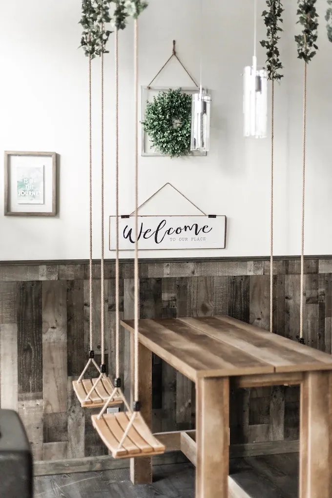 Inside Nella's Nutri-Bar: rope swings at a reclaimed-wood table under a “Welcome to our place” sign and hanging greenery